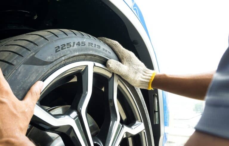 Close-up of a technician's gloved hand fitting a new car tire onto an alloy wheel during tire change service.