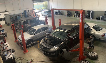 4 cars in for a service at Coleman Tyres and Mechanical. One car is jacked up, while another is waiting to be