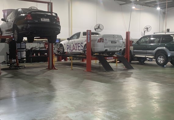 3 cars in for a service, the two most left cars have been jacked up off the ground