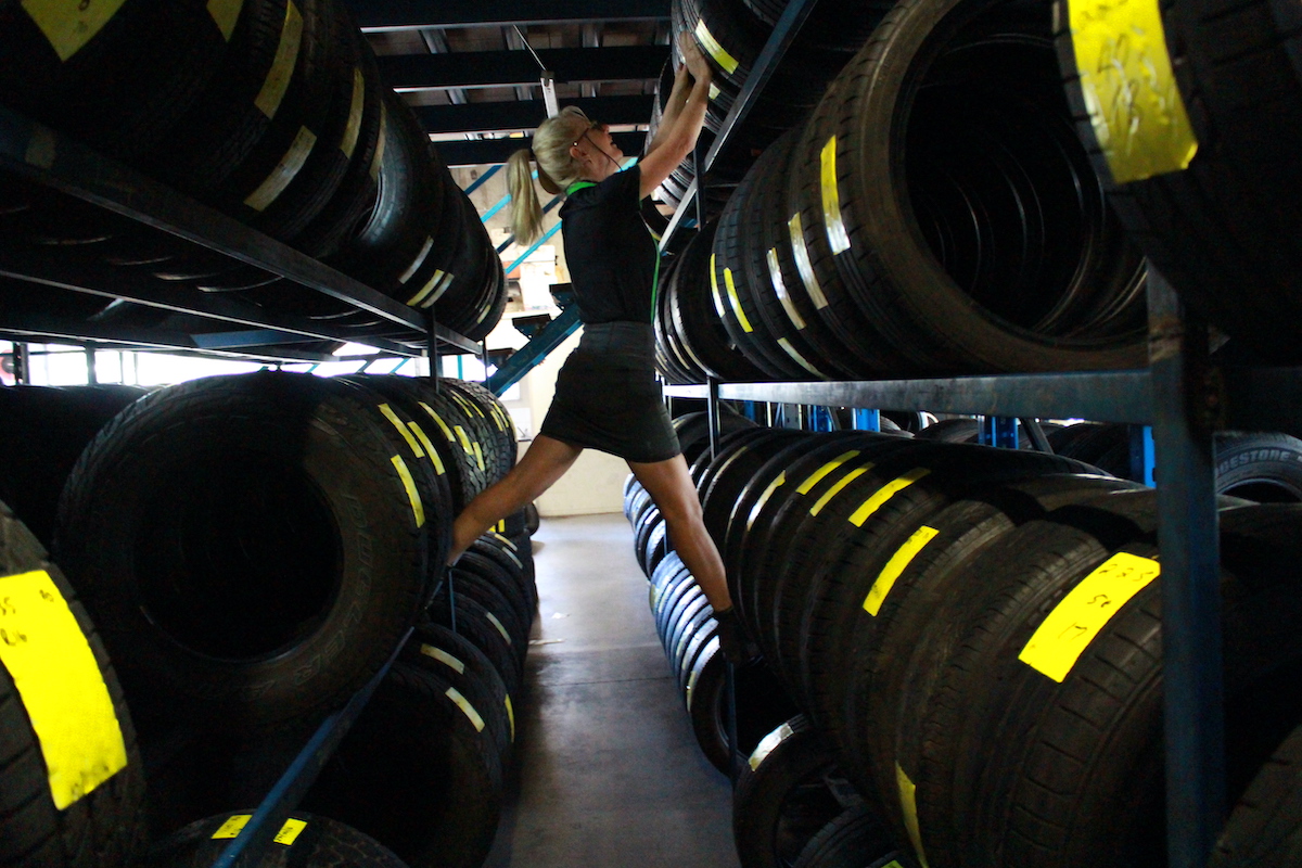 A Coleman Tyres & Mechanical employee finding a tyre. She is surrounded by a lot of tyres and is standing on the racks to see the one she's looking for.