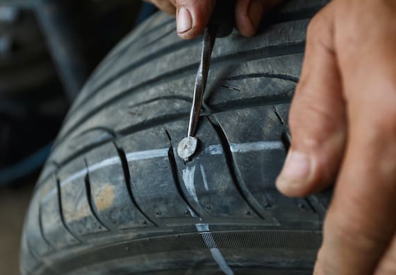 Puncture repairman fixing car's tire trying to remove nail from hole.